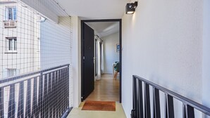 Un pasillo estrecho con suelo de madera, una puerta negra al final y una pequeña alfombra en la entrada.