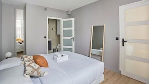 A modern bedroom with a large bed, a walk-in closet, a bathroom with a mirror, and a door with frosted glass panels. - Charming Apartment in the Center of Paris / Bourse (Paris)