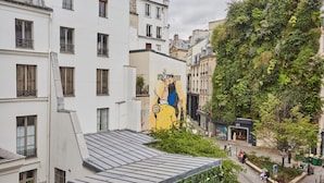A building with a mural on the side, a tree-covered wall, and a street with pedestrians. - Charming Apartment in the Center of Paris / Bourse (Paris)