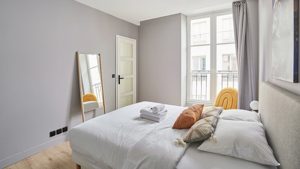 A bedroom with a bed, a mirror, a window with curtains, and a door. - Charming Apartment in the Center of Paris / Bourse (Paris)