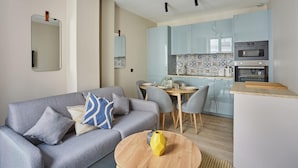 A modern living room with a grey sofa, a dining table with chairs, and a kitchen area with light blue cabinets and a built-in oven. - Charming Apartment in the Center of Paris / Bourse (Paris)