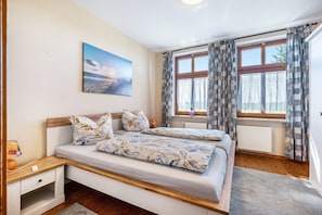 A bedroom with a bed, a nightstand, a window with curtains, a radiator, and a painting on the wall.