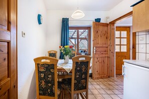 A dining area with a wooden table, chairs, a vase with flowers, and a window with curtains.