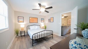 A bedroom with a bed, bedside tables, a ceiling fan, and framed artwork on the walls.