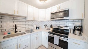 A modern kitchen with white cabinets, a stainless steel microwave, an oven, and a sink. - OV Mosaic - Drift Suite (Norfolk)