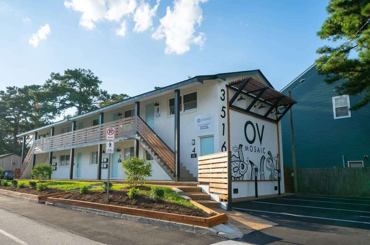 A motel with a staircase leading to the entrance, numbered rooms, a no parking sign, and a mosaic mural on the side.