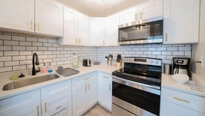 A modern kitchen with white cabinets, a stainless steel oven, a microwave, and a sink. - OV Mosaic - Summer Suite (Norfolk)