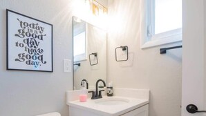 A bathroom with a toilet, sink, and mirror. There is a motivational quote on the wall and a window above the sink. - OV Mosaic - Summer Suite (Norfolk)