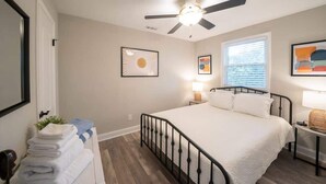 A bedroom with a bed, a ceiling fan, a window with blinds, and artwork on the walls. - OV Mosaic - Sienna Suite (Norfolk)