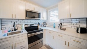 A modern kitchen with white cabinets, a stainless steel microwave, a gas stove, and a sink. - OV Mosaic - Sienna Suite (Norfolk)
