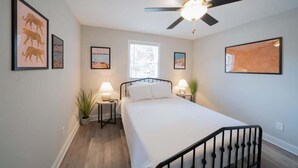 Ein Schlafzimmer mit einem Bett, zwei Nachttischen mit Lampen, einem Deckenventilator und gerahmten Kunstwerken an den Wänden.