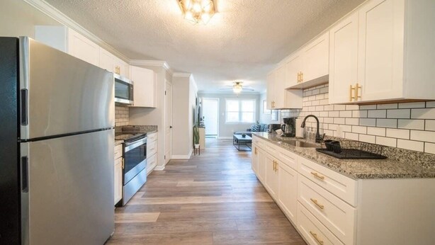 A spacious kitchen with white cabinetry, a stainless steel refrigerator, and a granite countertop. - OV Mosaic - Buoy Suite (Norfolk)