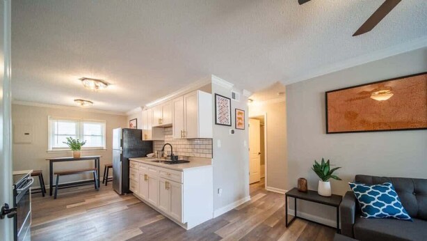 A modern kitchen with white cabinets, a dining area with a bench, and a living room with a sofa and a coffee table.