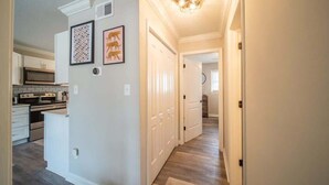 A hallway with a wooden floor, white walls, and a ceiling light fixture.