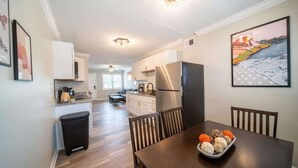 A modern kitchen with white cabinets, stainless steel appliances, and a dining area with a wooden table and chairs. - OV Mosaic - River Suite (Norfolk)