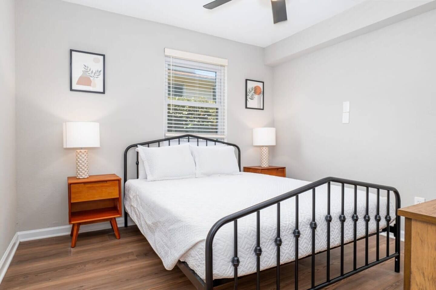 A bedroom with a single bed, two bedside tables, a window with blinds, and a ceiling fan.