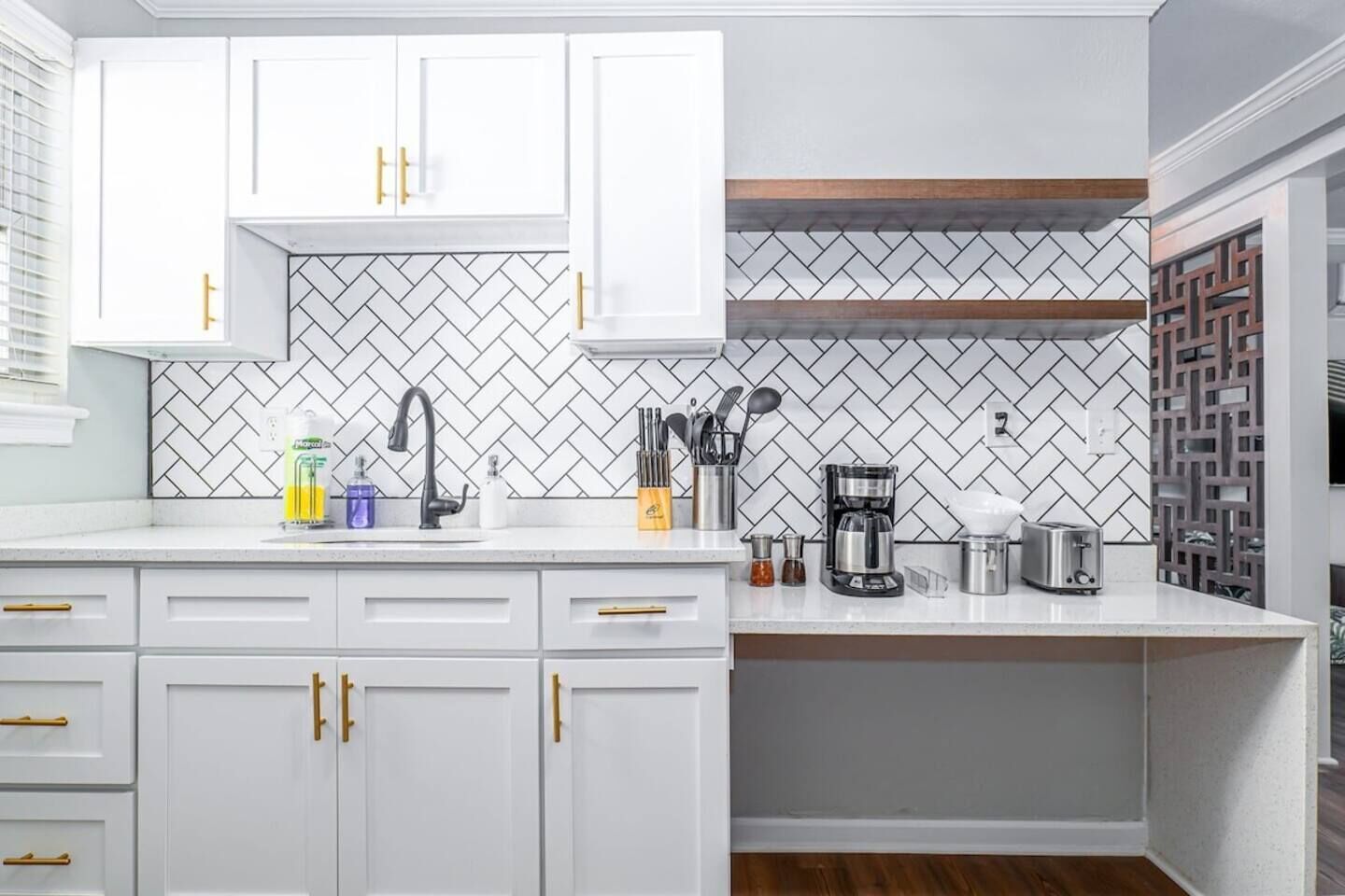 A modern kitchen with white cabinets, a herringbone tile backsplash, and a coffee maker on the counter.