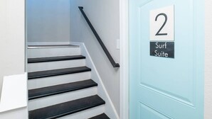 A staircase with black steps leading to a light blue door marked with the number 2 and labeled "Surf Suite".