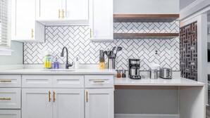 A modern kitchen with white cabinets, a herringbone tile backsplash, and a coffee maker on the counter.