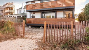 A modern two-story house with a wooden deck and a sandy driveway.