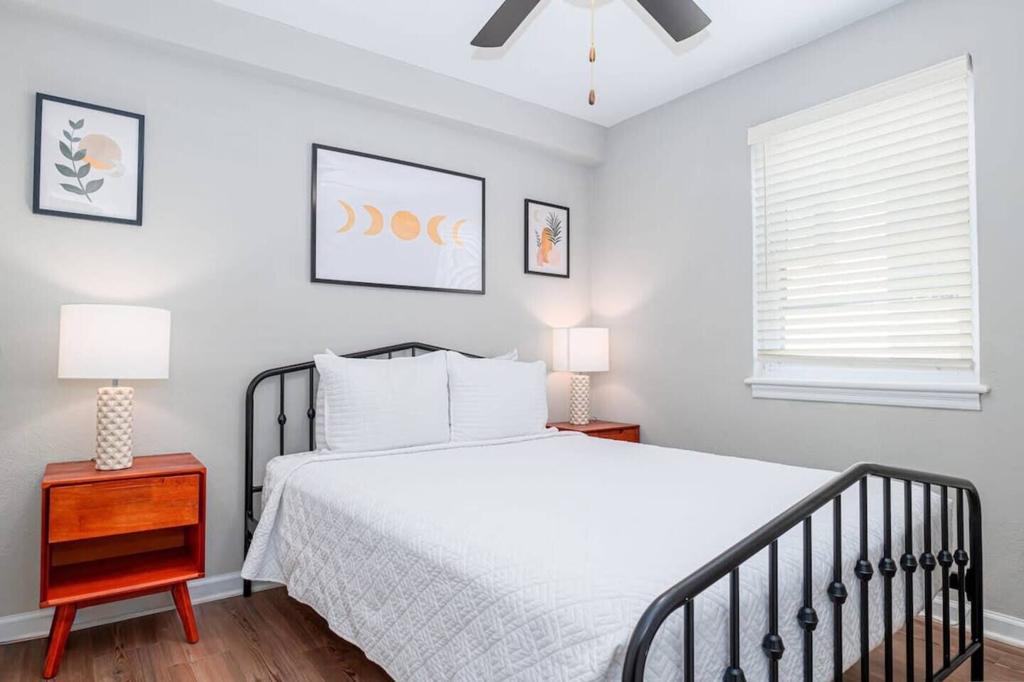 A bedroom with a bed, two bedside tables, a ceiling fan, and a window with blinds.
