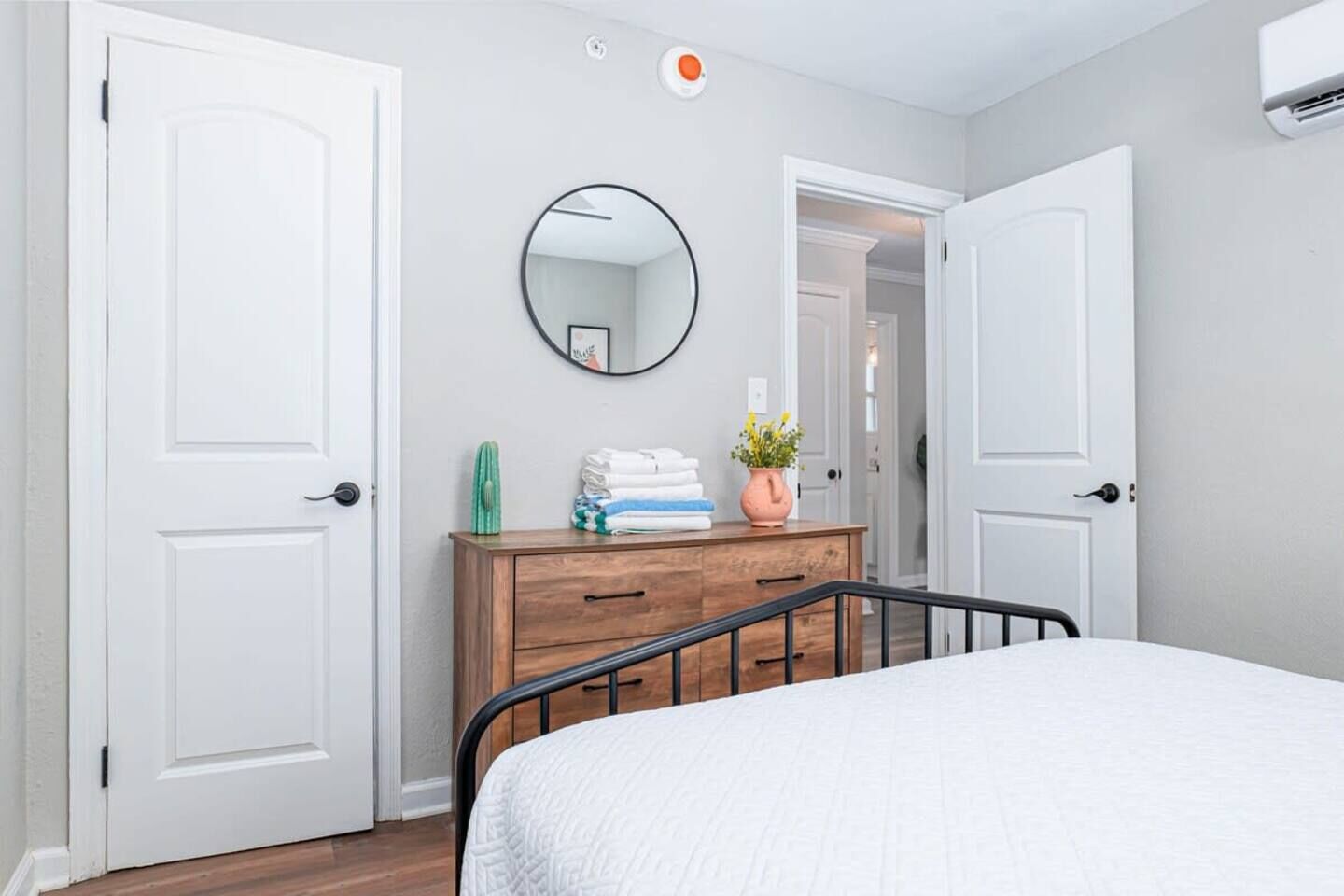 Une chambre à coucher avec un lit, une commode, un miroir et deux portes blanches.