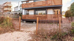 A modern two-story house with a wooden deck and a sandy driveway.