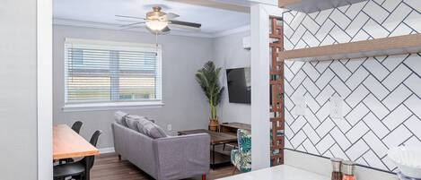 A modern living room with a grey sofa, wooden dining table, and a ceiling fan.