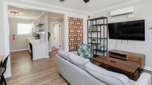 A modern living room with a ceiling fan, a flat-screen TV, a wooden coffee table, and a grey sofa. - 1866 EOV Wave Suite (Norfolk)