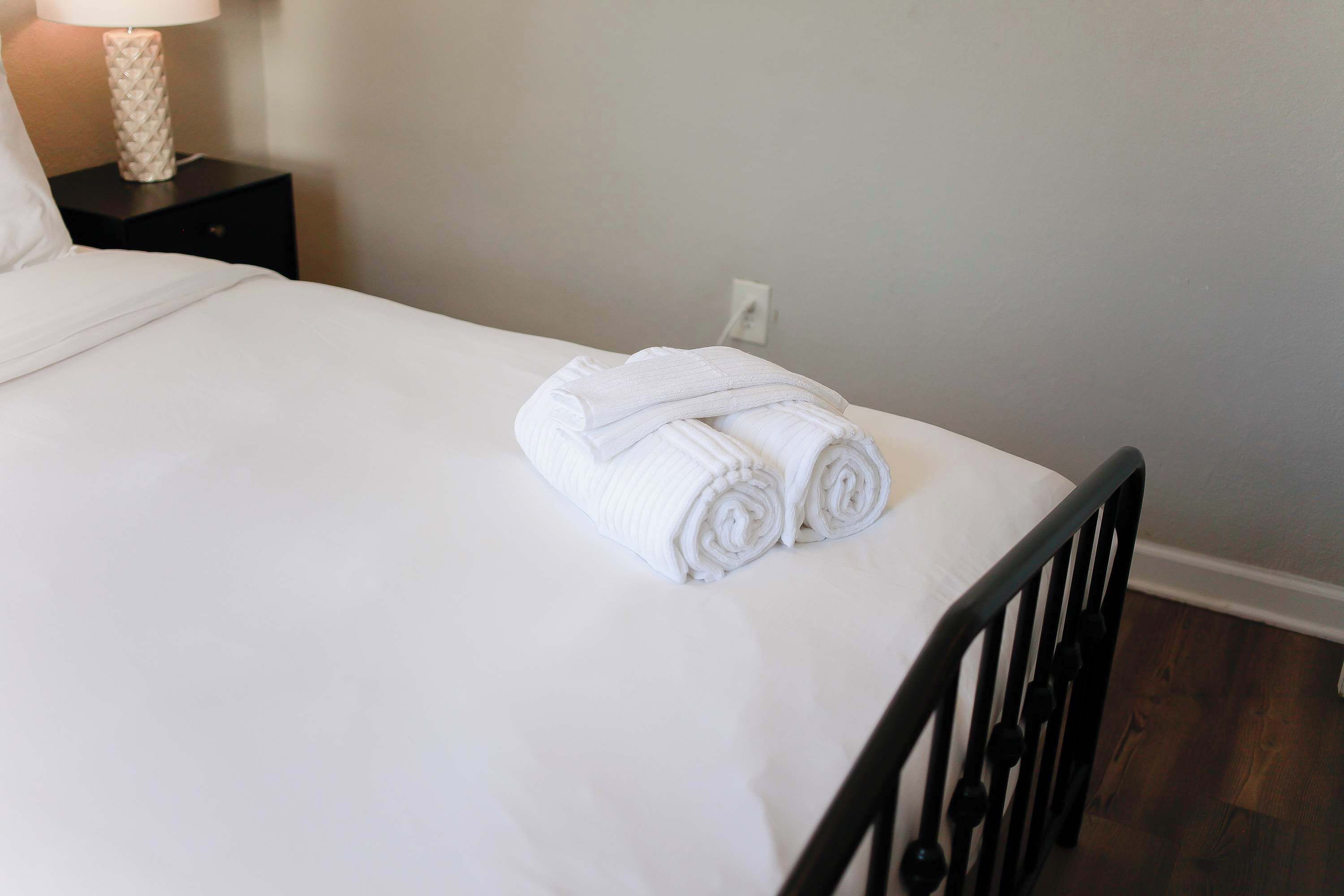 A neatly made bed with white linens and a rolled towel on top.
