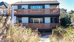 Een modern huis met twee verdiepingen en een balkon, omgeven door natuurlijke begroeiing.