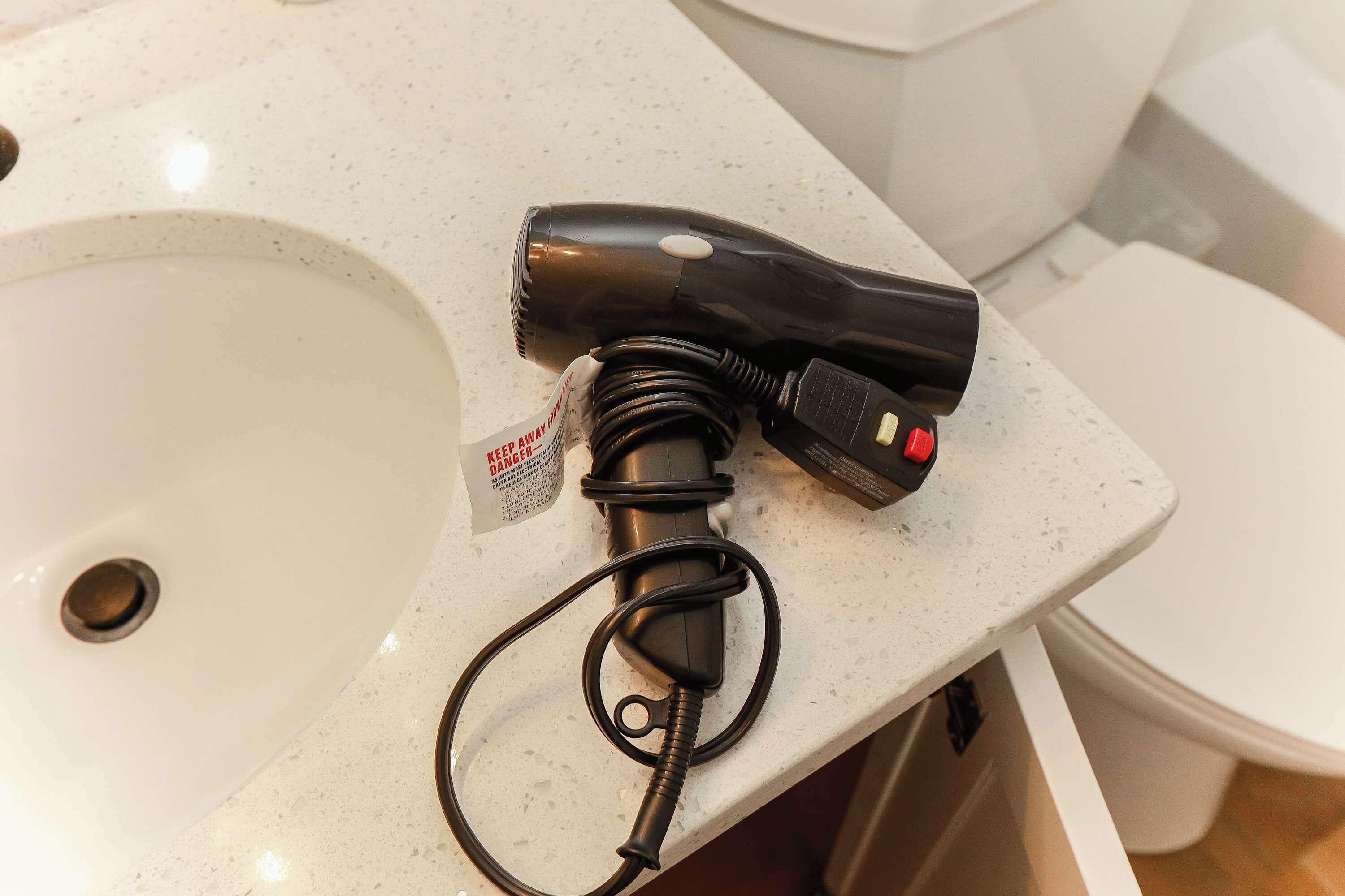 Un lavabo et des toilettes dans la salle de bain, avec un sèche-cheveux posé sur le comptoir.