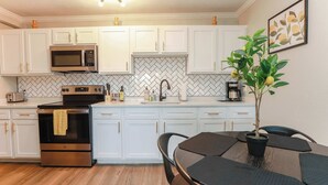 A modern kitchen with white cabinets, stainless steel appliances, and a wooden floor.