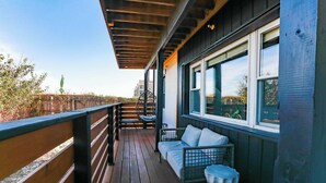 A wooden deck with a sofa and chairs, a railing, and a view of a bridge and trees.