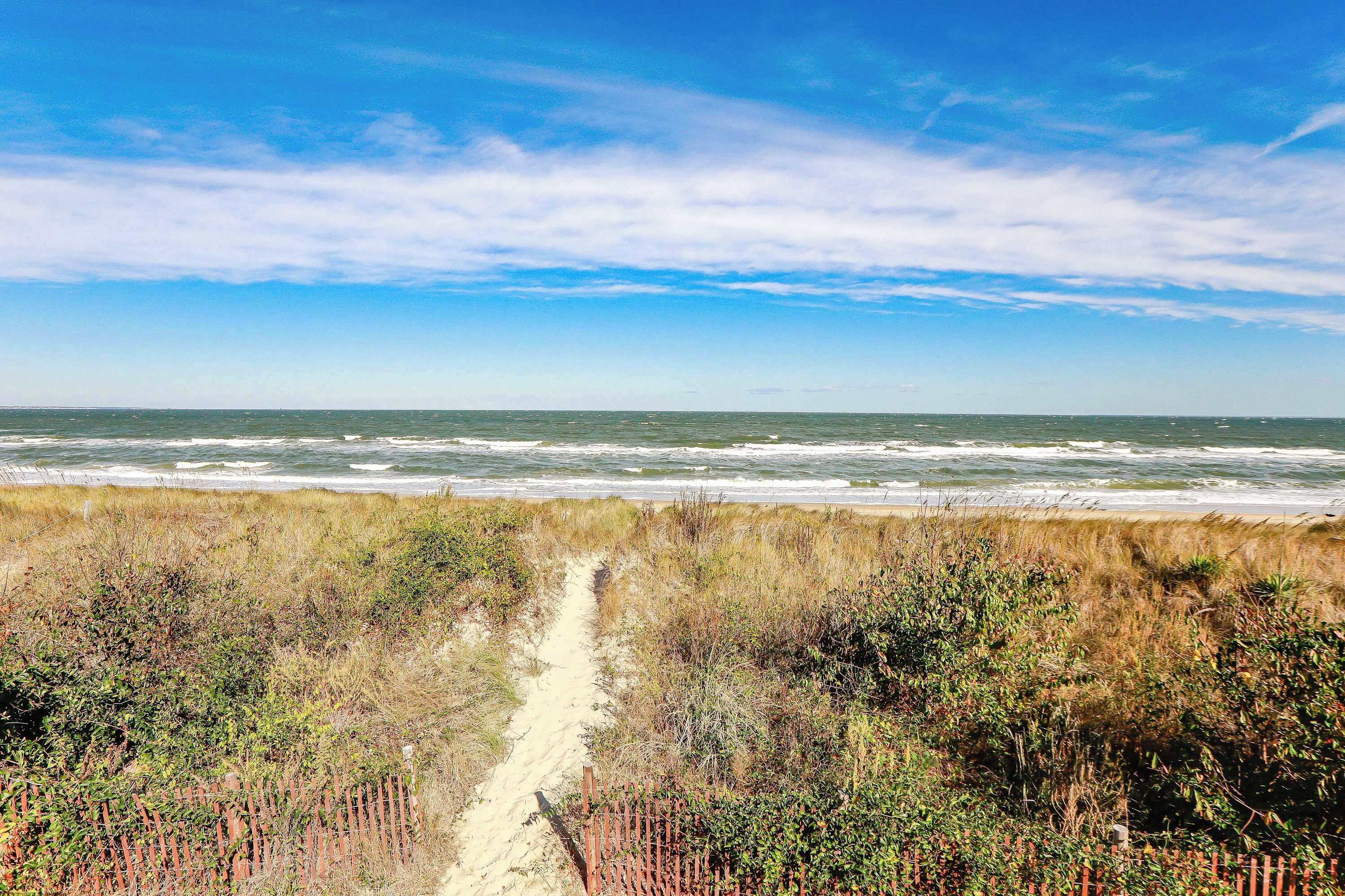Ein Strandweg, der zum Meer führt, mit blauem Himmel.