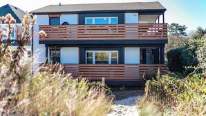 A modern two-story house with a balcony, large windows, and a pathway leading to the entrance.