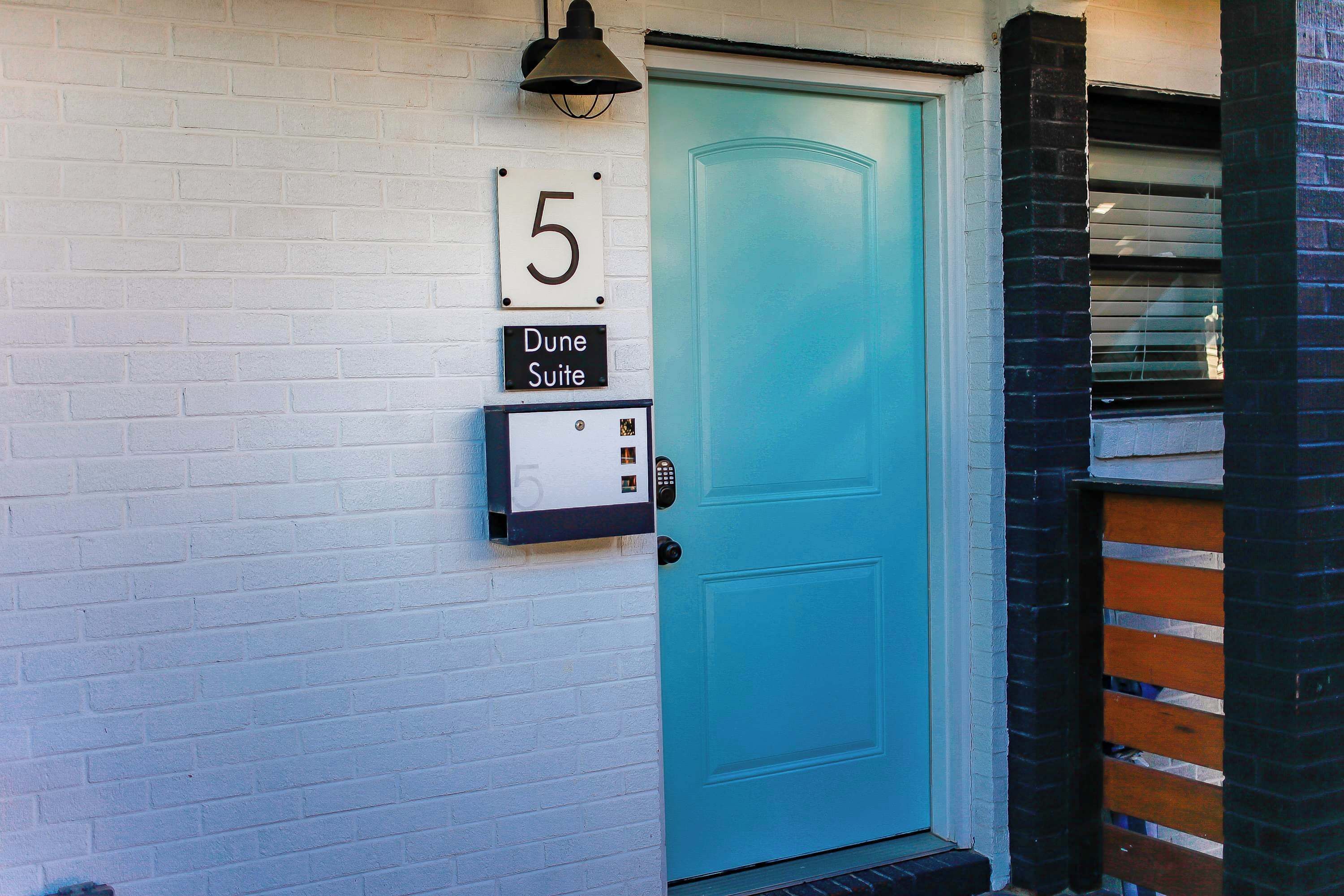 Una puerta turquesa con un letrero con el número 5 arriba y una placa que dice 'Dune Suite' debajo.