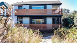 A modern two-story house with a balcony, surrounded by natural vegetation.