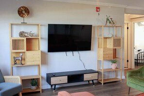 Un soggiorno moderno con una TV a schermo piatto, scaffali in legno, un divano e una poltrona verde.
