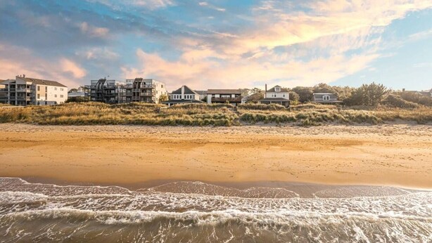 A beachfront property with multiple buildings, including a large multi-story structure and several single-story houses, with a sandy beach and ocean in the foreground.