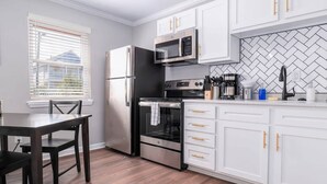 A modern kitchen with white cabinets, a stainless steel refrigerator, a microwave, an oven, and a coffee maker.