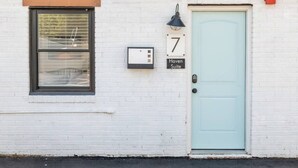 A white brick building with a light blue door, a window with blinds, and a sign indicating '7 Haven Suite'.