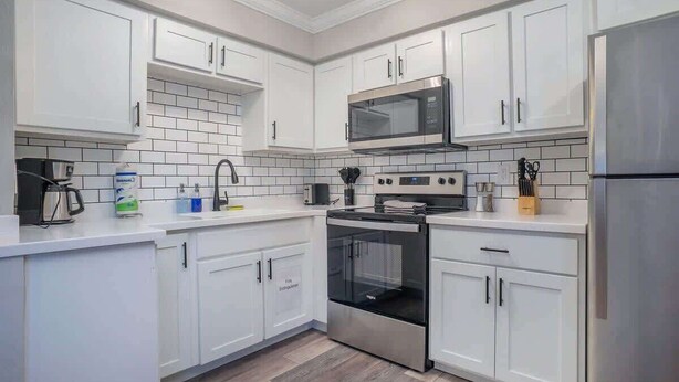 A modern kitchen with white cabinets, a stainless steel refrigerator, a microwave, an oven, and a coffee maker.