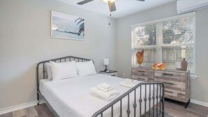 A bedroom with a bed, bedside table, lamp, dresser, and a ceiling fan.