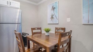 A dining area with a wooden table and chairs, a refrigerator, and two framed pictures on the wall.