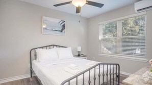 Ein Schlafzimmer mit einem Bett, einem Deckenventilator, einem Fenster mit Jalousien und einem Bild an der Wand.