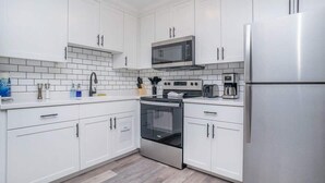 Eine moderne Küche mit weißen Schränken, einem Edelstahl-Kühlschrank, einer Mikrowelle, einem Backofen und einer Kaffeemaschine.