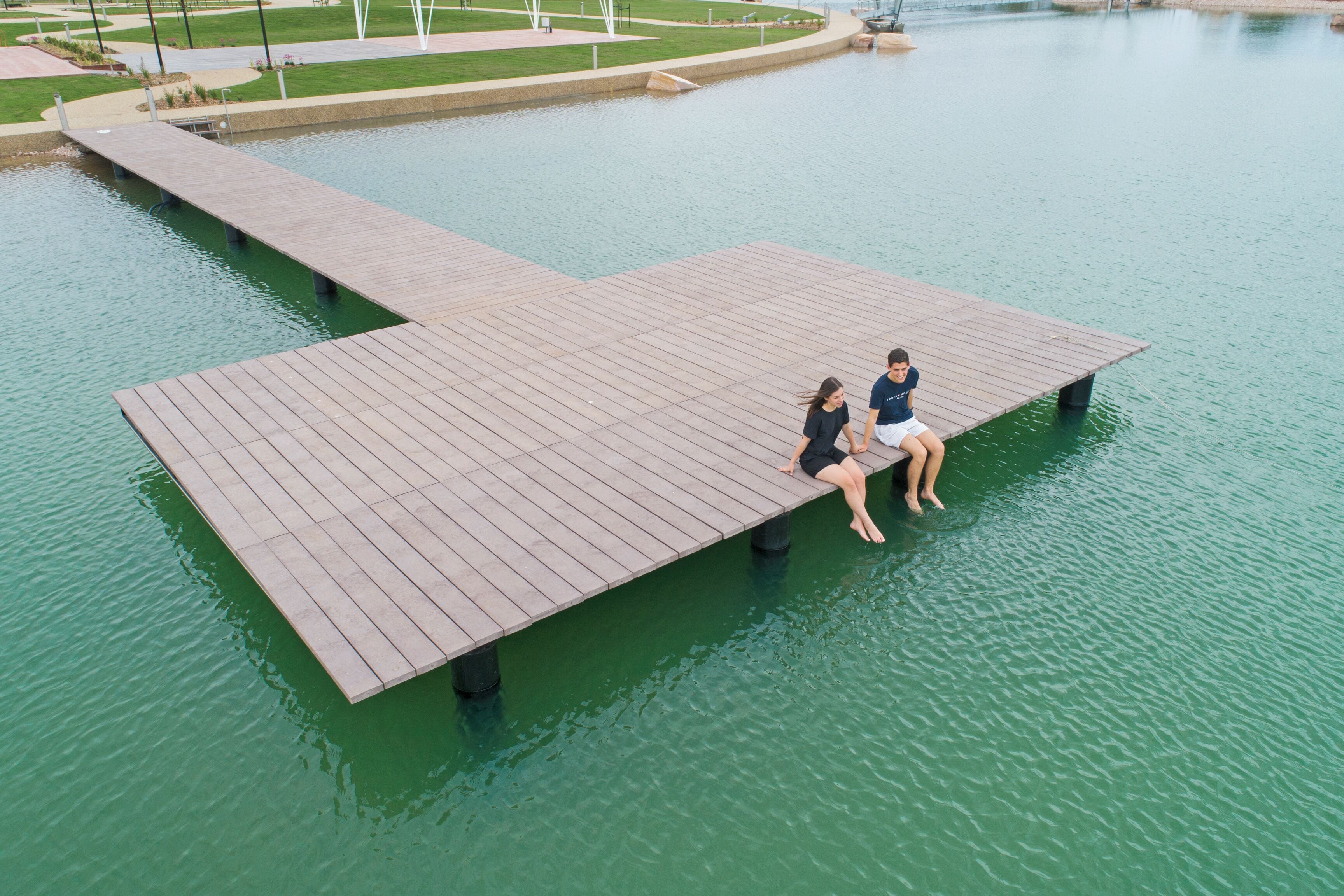 A wooden dock extending over calm water, with two people sitting on it.