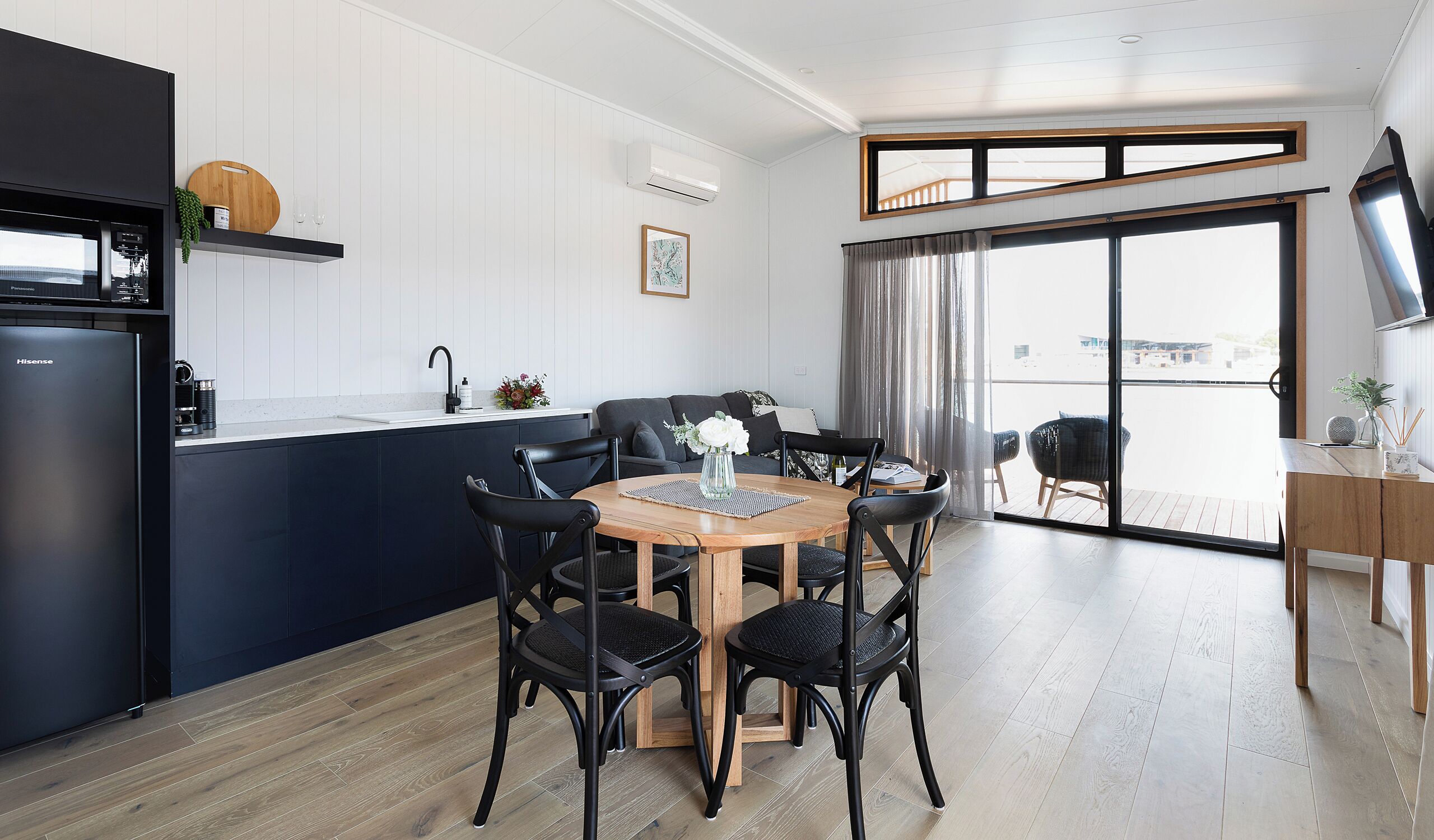 Una cocina moderna con refrigerador empotrado, un comedor con mesa y sillas de madera, y un amplio ventanal corredero que da a un balcón.