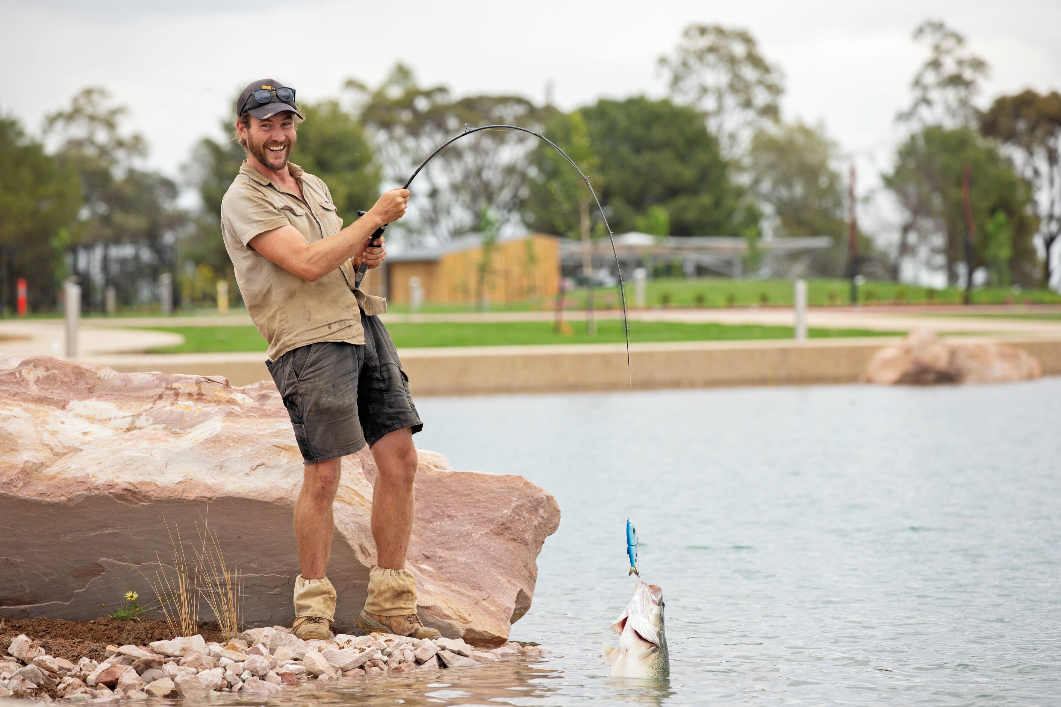 A man fishing by a rocky shore with a fish in the water.